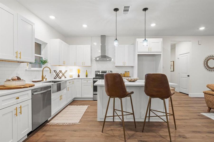 Kitchen with wall chimney exhaust hood, light hardwood / wood-style flooring, decorative light fixtures, white cabinetry, and appliances with stainless steel finishes