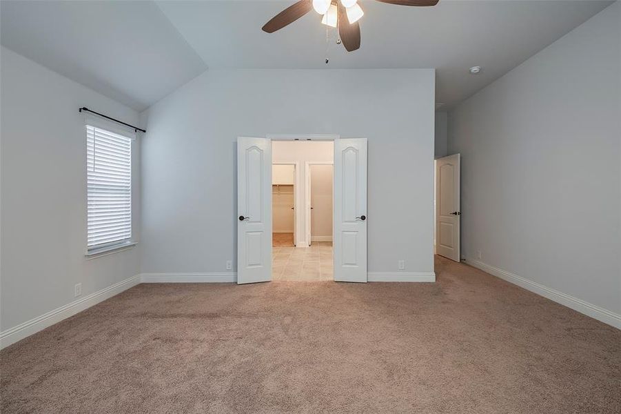 Unfurnished bedroom with ceiling fan, vaulted ceiling, and light colored carpet