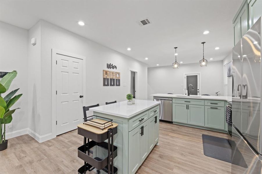 Kitchen with appliances with stainless steel finishes, sink, a kitchen island, hanging light fixtures, and light hardwood / wood-style floors