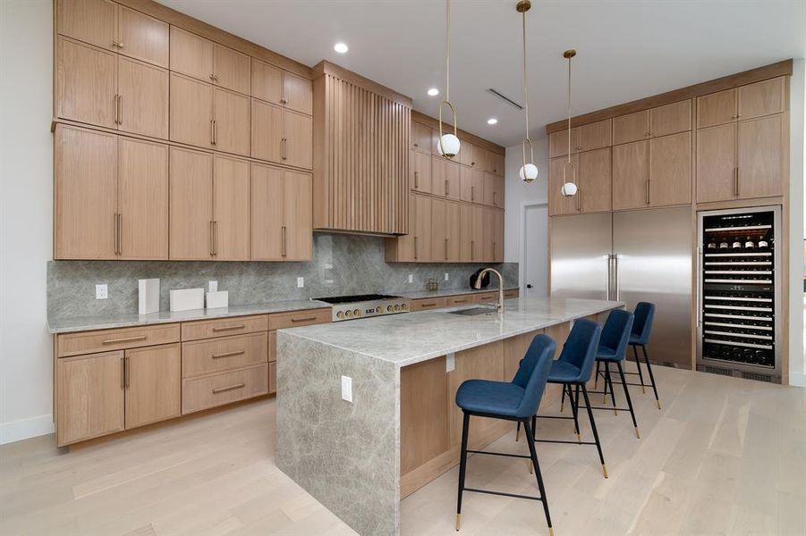 Kitchen featuring light stone countertops, a center island with sink, light hardwood / wood-style flooring, beverage cooler, and sink