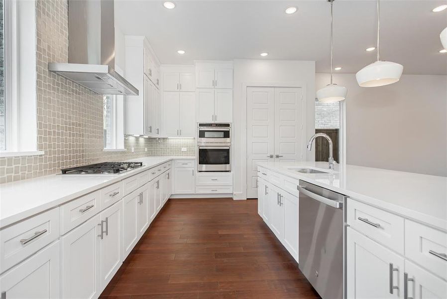 Kitchen with dark hardwood / wood-style floors, stainless steel appliances, wall chimney exhaust hood, decorative backsplash, and sink