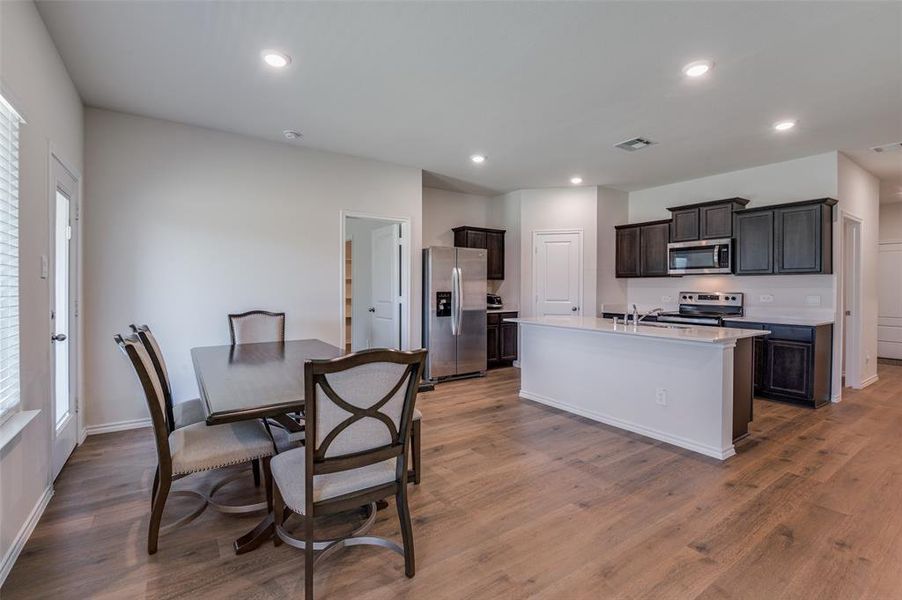 Kitchen with dark brown cabinets, dark hardwood / wood-style floors, stainless steel appliances, and a center island with sink