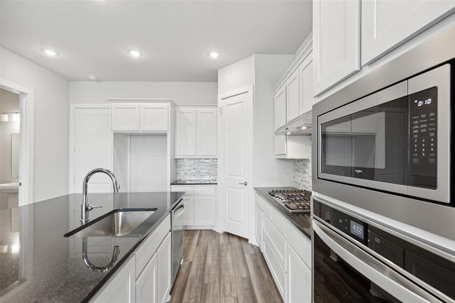 Kitchen with dark hardwood / wood-style floors, stainless steel appliances, dark stone countertops, backsplash, and sink