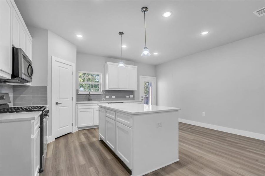 Kitchen with pendant lighting, wood-type flooring, white cabinetry, a kitchen island, and stainless steel appliances