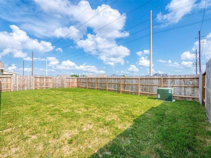 This expansive backyard with a sturdy fence provides ample space for outdoor activities, relaxation, and entertaining. The clear blue sky sets the scene for a perfect day enjoying the fresh air.