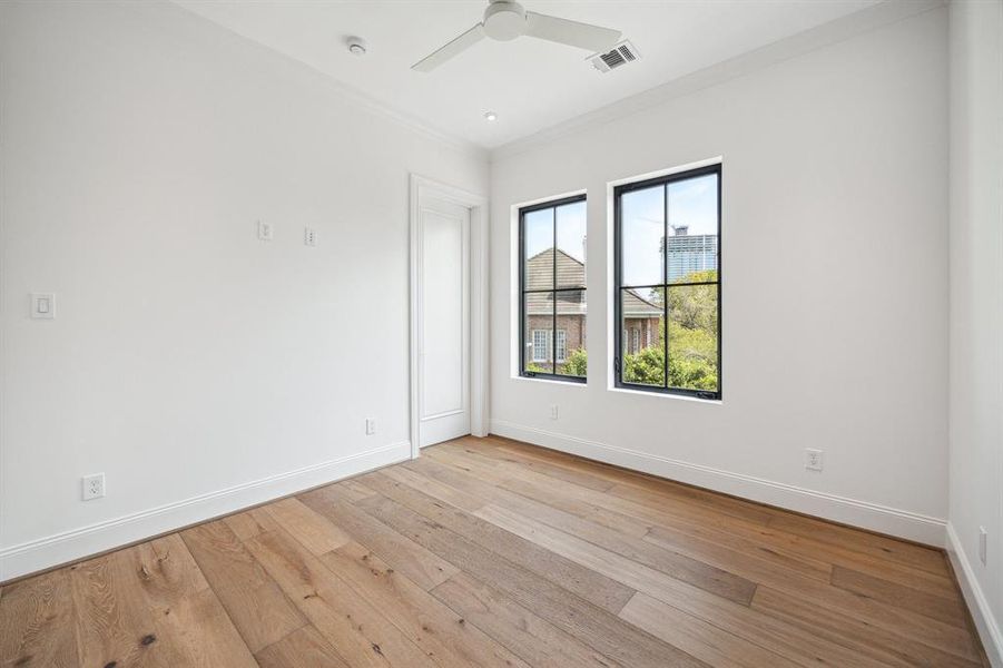 The second of four secondary bedrooms features European white oak flooring, a spacious walk-in closet, and a private ensuite bathroom. With a designer ceiling fan and bright Eastern exposures, the room is filled with natural light, offering both comfort and style.