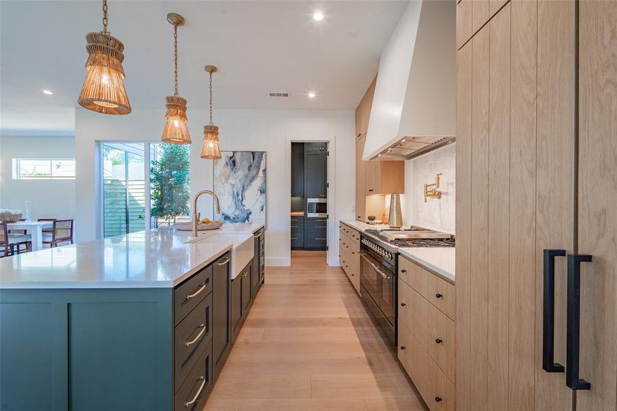 Kitchen with range with two ovens, decorative light fixtures, gray cabinets, premium range hood, and a center island with sink