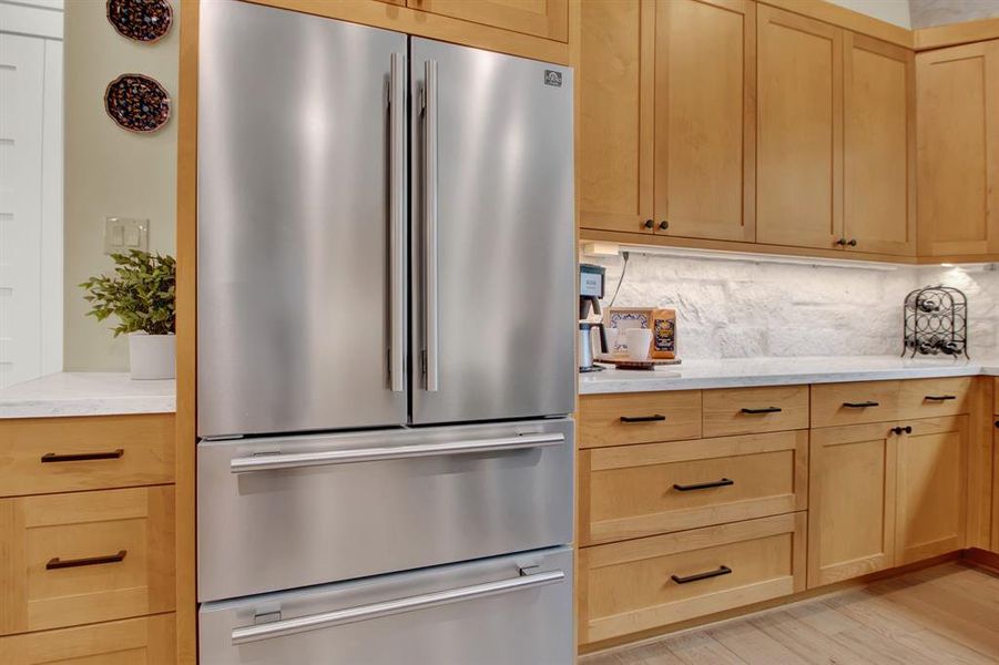 The kitchen also features modern stainless steel appliances, light wood cabinetry, and elegant stone backsplash, offering a sleek and inviting space for cooking and entertaining.