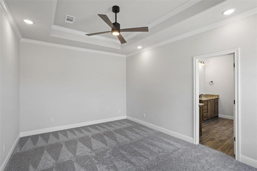 Empty room with a raised ceiling, ornamental molding, dark colored carpet, and ceiling fan