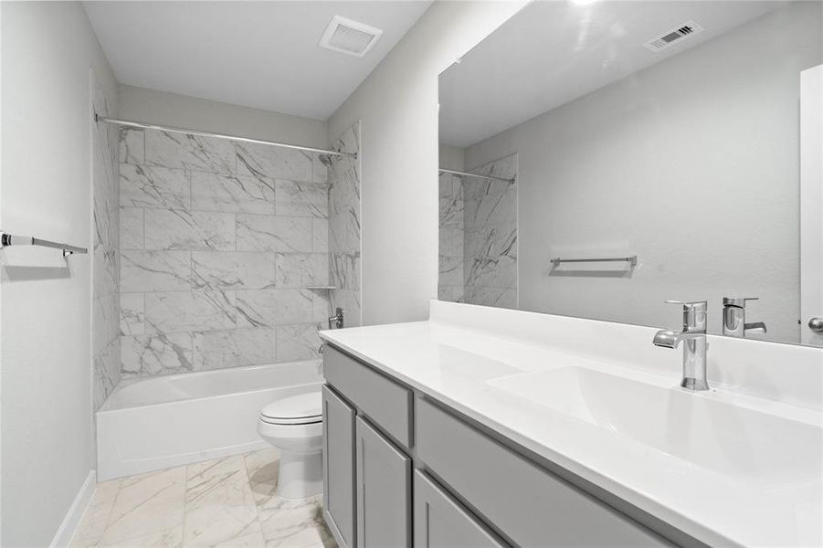 Secondary bath features tile flooring, bath/shower combo with tile surround, stained wood cabinets, beautiful light countertop, mirror, dark, sleek fixtures and modern finishes!