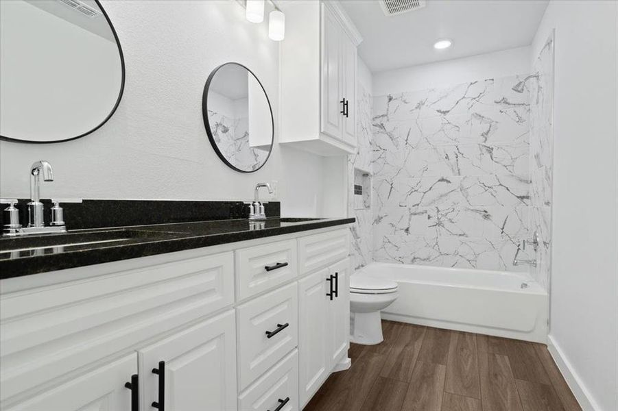 Full bathroom with dual bowl vanity, tiled shower / bath, hardwood / wood-style flooring, and toilet