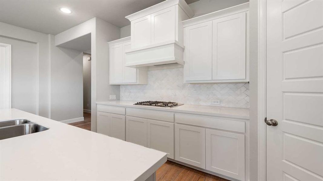 Kitchen featuring white cabinetry, backsplash, premium range hood, stainless steel gas cooktop, and wood-type flooring