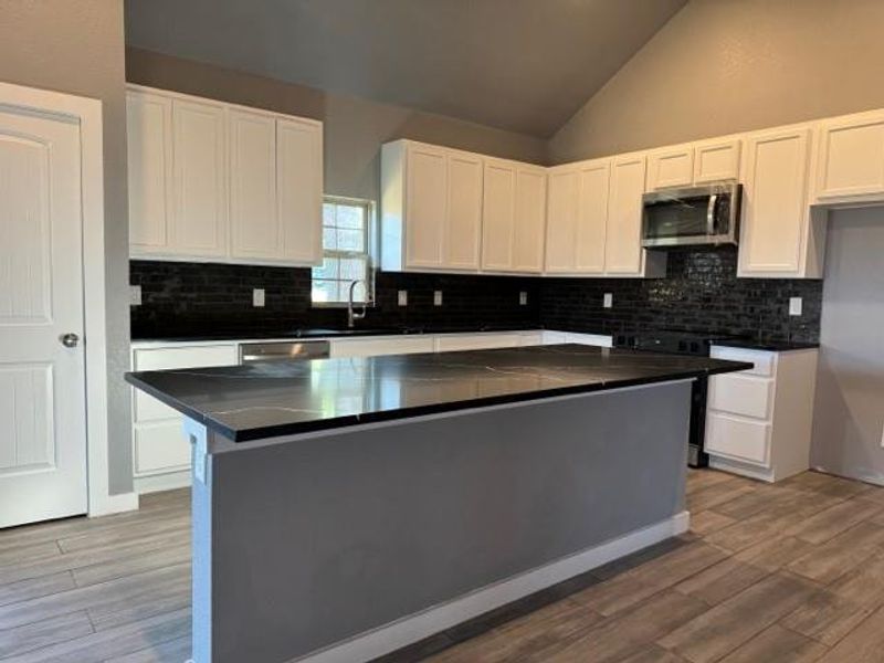 Kitchen featuring white cabinetry, backsplash, a kitchen island, and range with electric stovetop