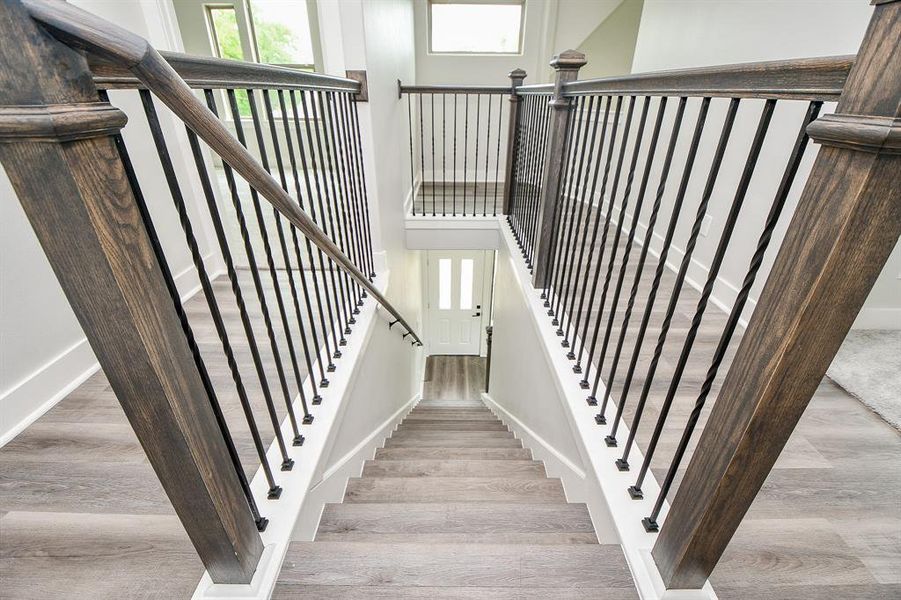 The photo showcases an elegant staircase with dark wood banisters and modern, black metal spindles, complemented by light gray wood flooring and crisp white walls.