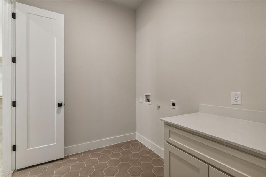 Laundry area with dark tile patterned floors, hookup for a washing machine, cabinets, and electric dryer hookup