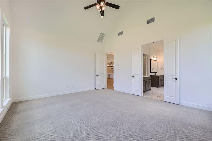 Unfurnished bedroom featuring multiple windows, ensuite bathroom, light carpet, ceiling fan, and high vaulted ceiling