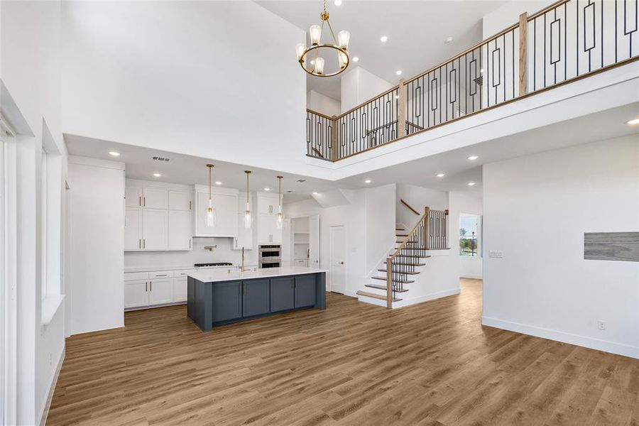 Kitchen with hanging light fixtures, white cabinetry, a kitchen island with sink, wood-type flooring, and a high ceiling