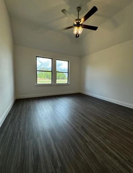 Spare room featuring ceiling fan, vaulted ceiling, and dark wood-type flooring