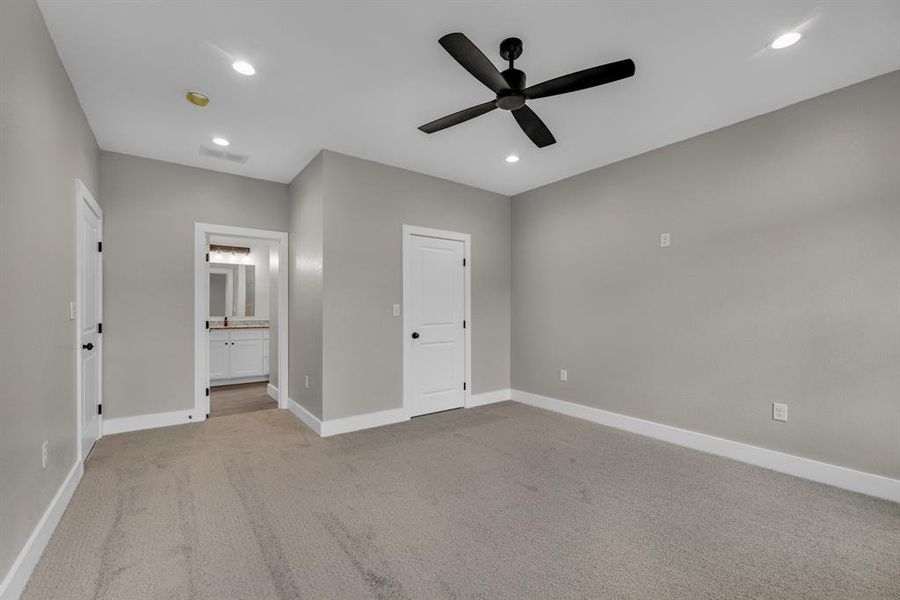 Unfurnished bedroom featuring ceiling fan, light colored carpet, and ensuite bath