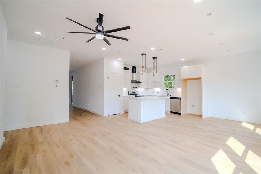 Kitchen with a center island, white cabinetry, ceiling fan, wall chimney range hood, and pendant lighting