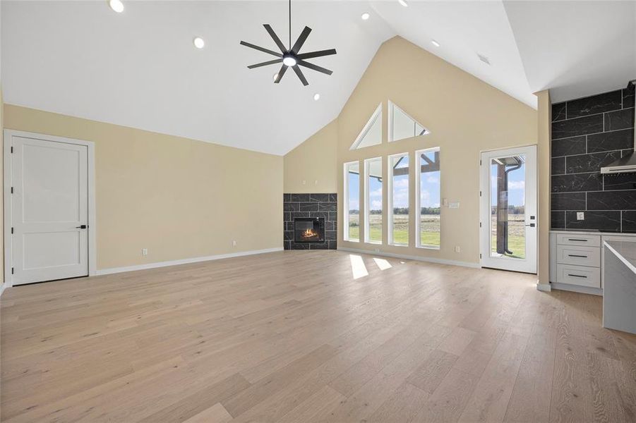 Unfurnished living room featuring ceiling fan, high vaulted ceiling, light wood-type flooring, and a fireplace