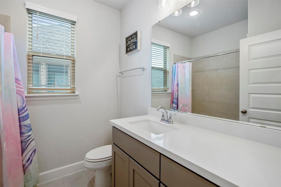 This full bathroom is located off the hall of the secondary bedrooms making it easy to share and get ready. It features a large vanity, gray cabinets, quartz countertops, and a combined shower and tub.