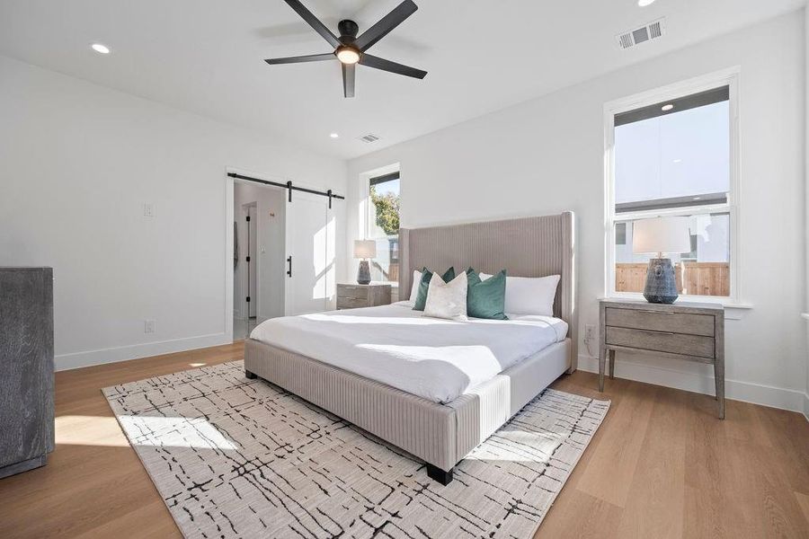 Bedroom with a barn door, light wood-type flooring, and ceiling fan