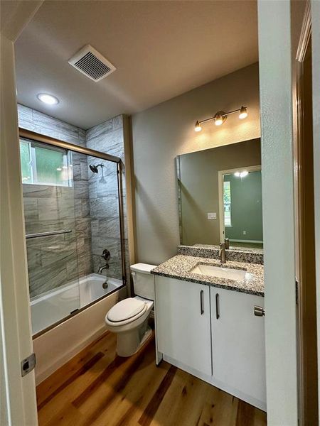 Full bathroom featuring hardwood / wood-style flooring, bath / shower combo with glass door, toilet, and vanity