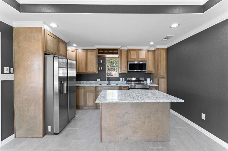 Kitchen with light stone counters, a kitchen island, appliances with stainless steel finishes, ornamental molding, and sink