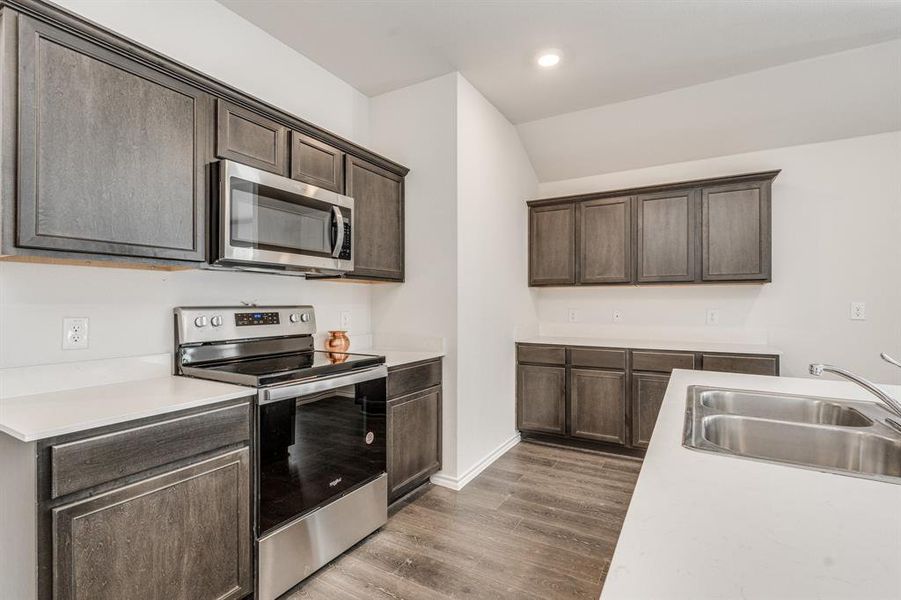 Kitchen with dark brown cabinets, sink, vaulted ceiling, appliances with stainless steel finishes, and dark hardwood / wood-style flooring