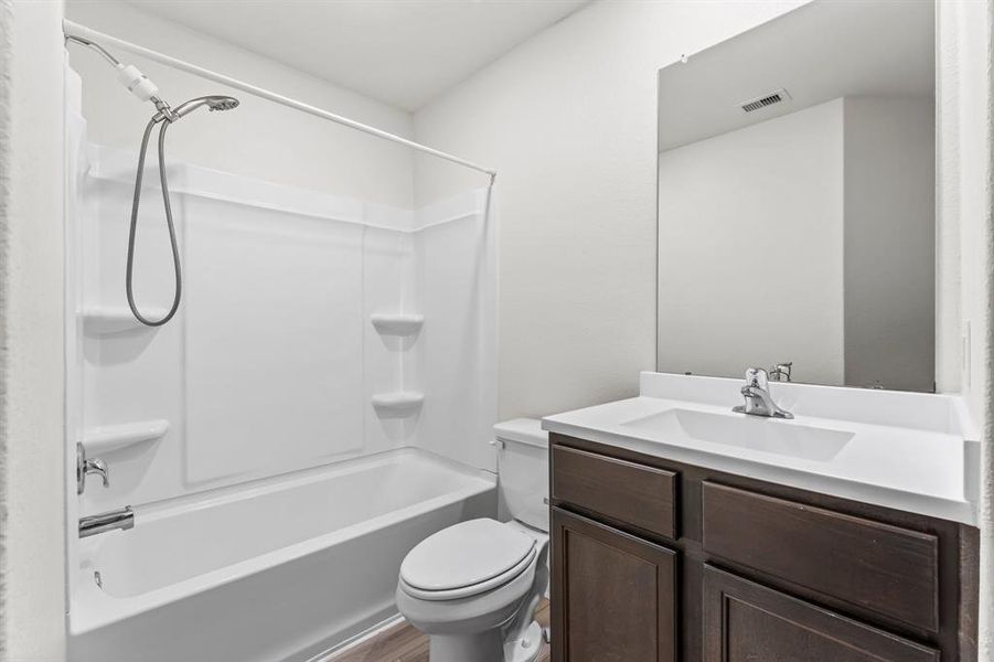 The second full bathroom for guests and Bedrooms 2 and 3 features wood-look vinyl plank flooring, single vanity with solid surface counter top and integrated bowl, toilet, and shower/tub combo with built-in shelves and removable hand-held shower head.