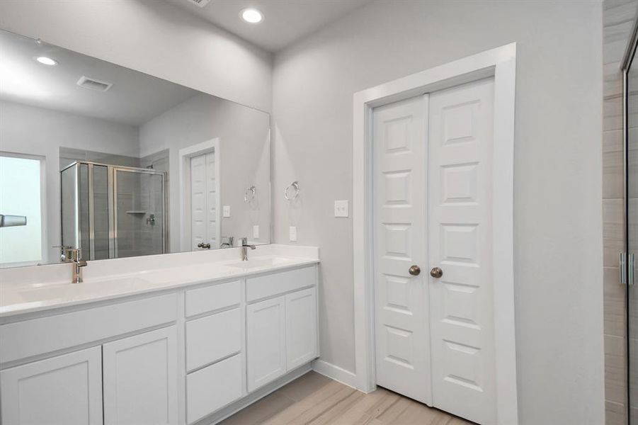 Revel in the expansive walk-in shower surrounded by tasteful tile, unwind in a separate garden tub adorned with personalized detailing, and elevate your daily rituals at the sophisticated vanity, equipped with double sinks, light-hued countertops, contemporary hardware, and bright recessed lights.