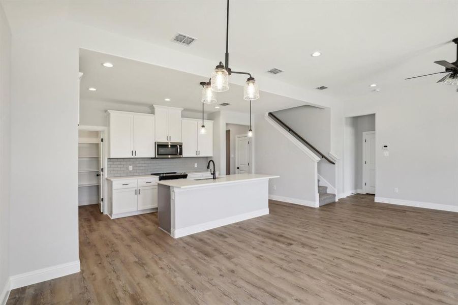 Kitchen with ceiling fan, decorative backsplash, pendant lighting, an island with sink, and light hardwood / wood-style floors