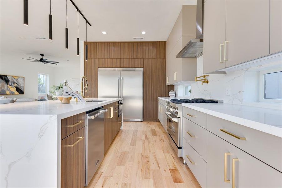 Kitchen with ceiling fan, light stone counters, light wood-type flooring, wall chimney range hood, and high quality appliances