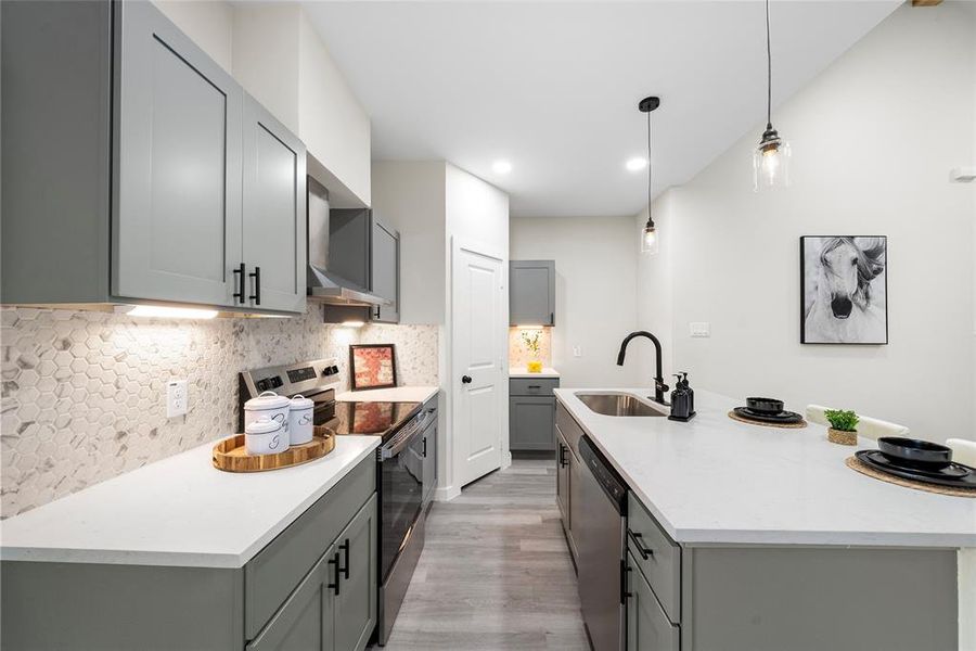 Kitchen with stainless steel appliances, sink, pendant lighting, gray cabinets, and light hardwood / wood-style floors