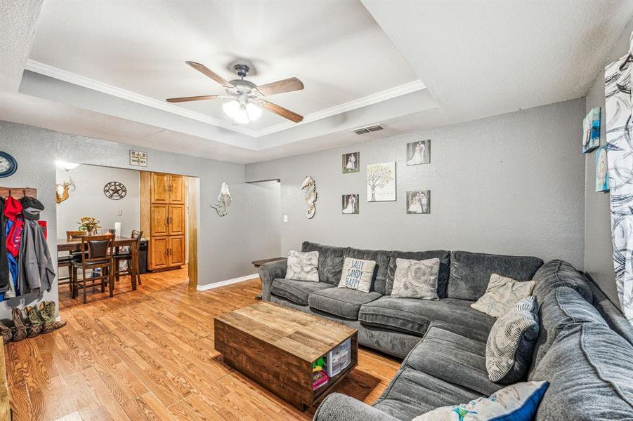 Living room with ceiling fan, ornamental molding, light hardwood / wood-style flooring, and a tray ceiling