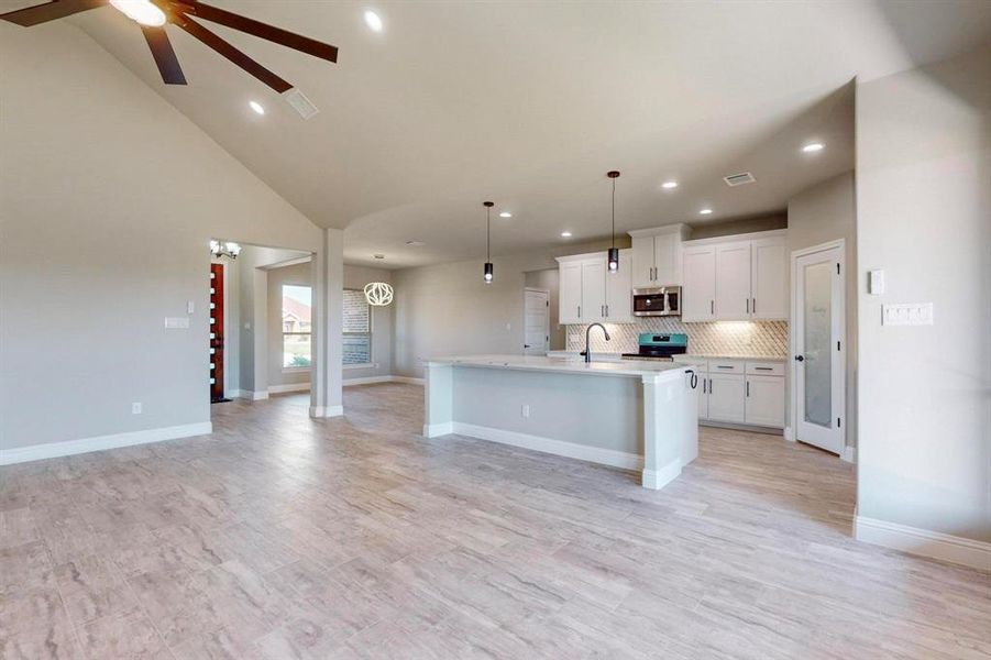 Kitchen with a kitchen island with sink, white cabinetry, hanging light fixtures, stainless steel appliances, and ceiling fan