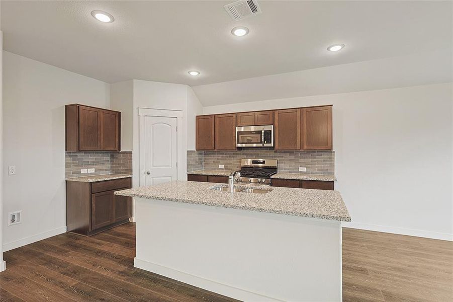 Kitchen with dark wood-type flooring, appliances with stainless steel finishes, a kitchen island with sink, and tasteful backsplash