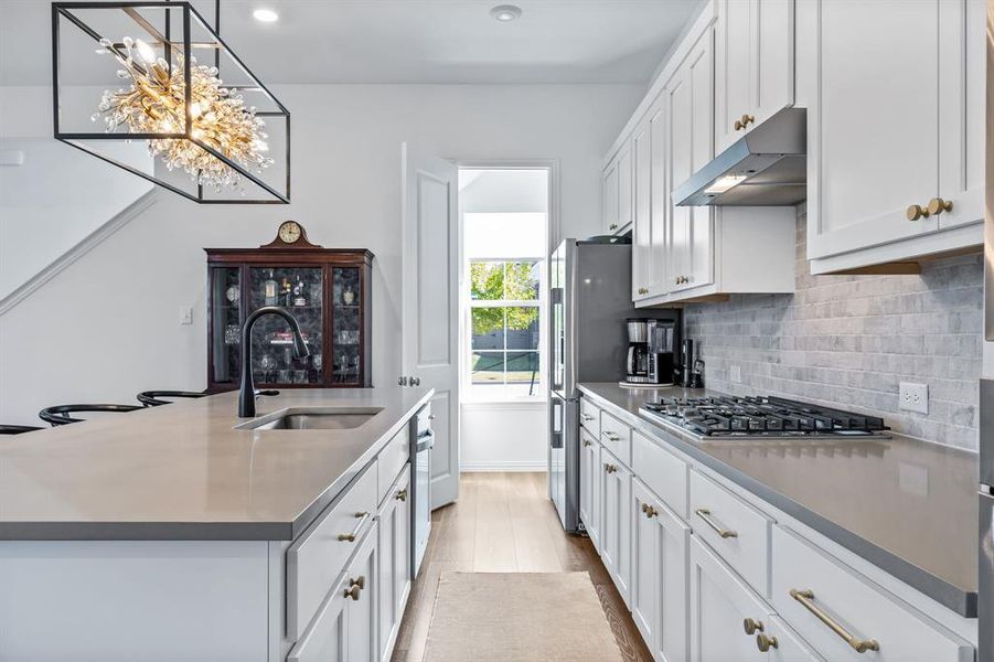 Kitchen featuring white cabinets, hanging light fixtures, sink, light hardwood / wood-style flooring, and appliances with stainless steel finishes