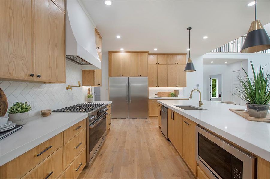 Kitchen with built in appliances, decorative light fixtures, light hardwood / wood-style flooring, custom range hood, and sink