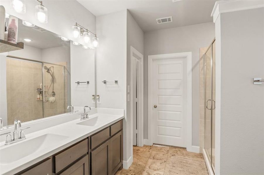 Bathroom featuring a shower with shower door, double sink vanity, and tile patterned flooring