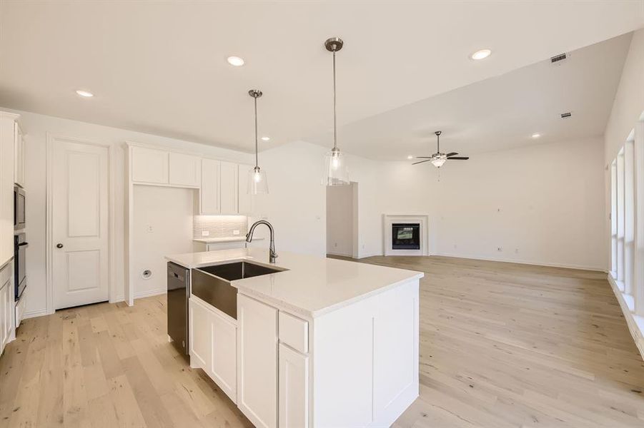 Kitchen with white cabinets, stainless steel appliances, a kitchen island with sink, and light wood-type flooring