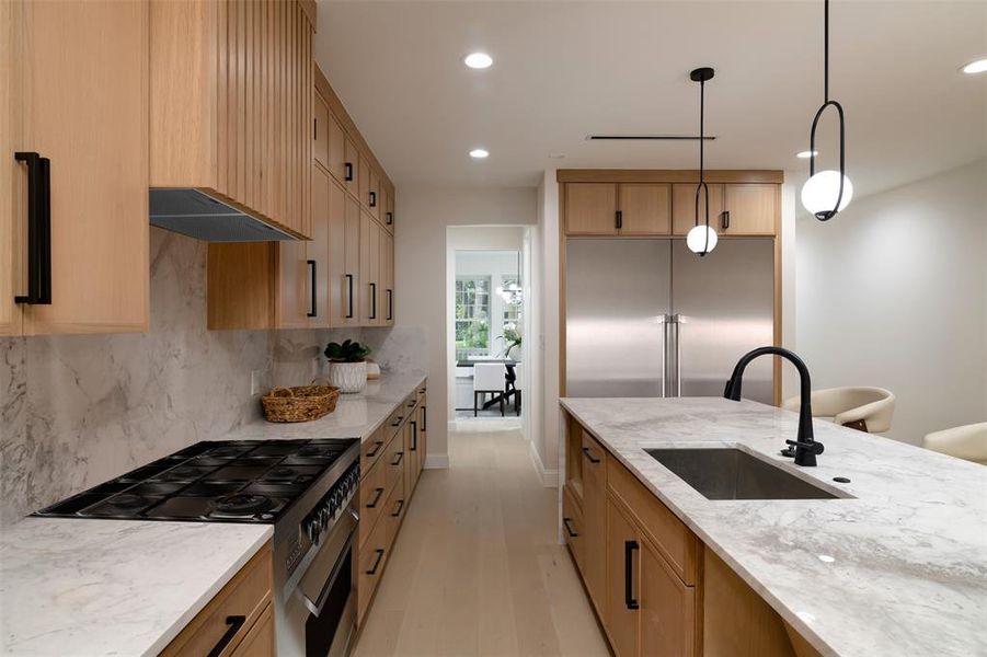 Kitchen with light wood-type flooring, light stone counters, sink, extractor fan, and pendant lighting