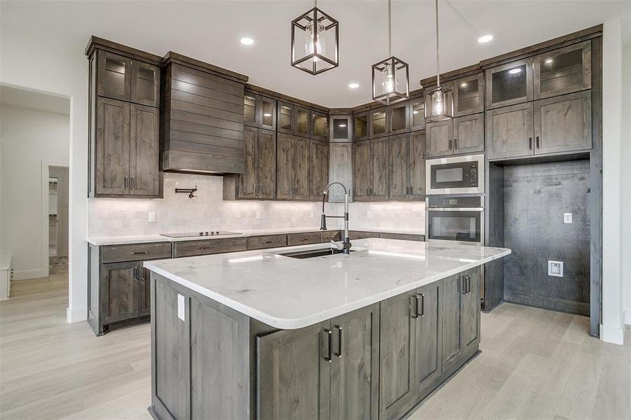 Kitchen with a center island with sink, stainless steel appliances, light wood-type flooring, and custom range hood