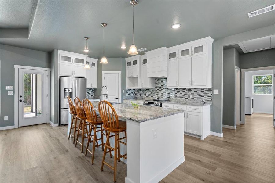 Kitchen featuring a breakfast bar area, light hardwood / wood-style flooring, appliances with stainless steel finishes, a kitchen island with sink, and white cabinetry