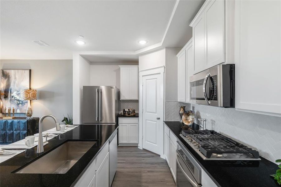 Kitchen with dark hardwood / wood-style flooring, backsplash, stainless steel appliances, sink, and white cabinetry