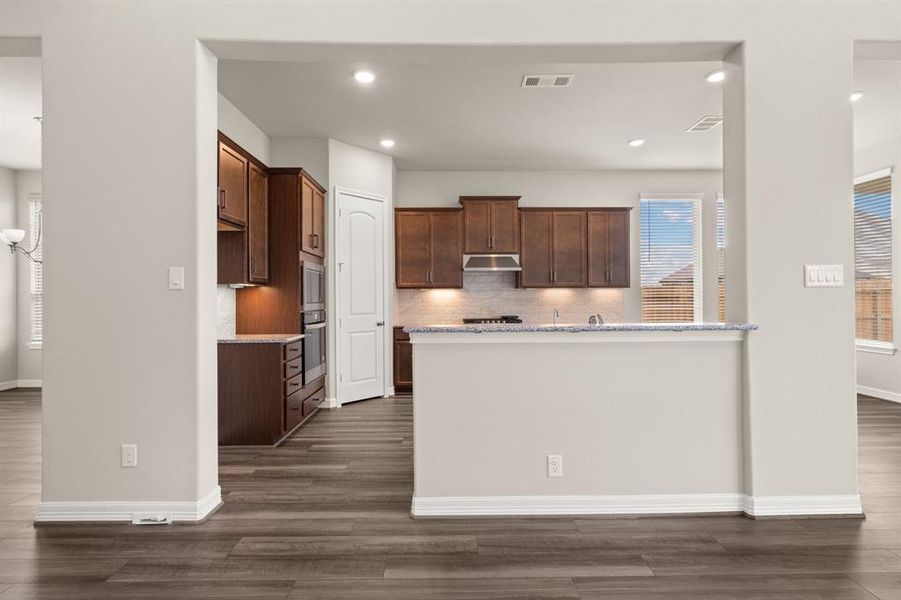 This light and bright kitchen features a large quartz island, dark stained cabinets, a large sink overlooking your family room, recessed lighting, and beautiful backsplash.