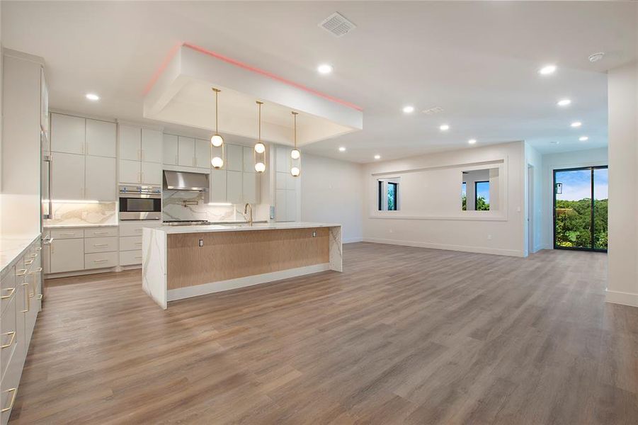Kitchen featuring appliances with stainless steel finishes, hardwood / wood-style floors, pendant lighting, backsplash, and a kitchen island with sink