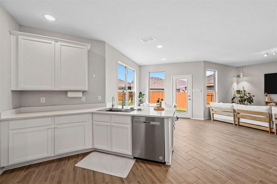 Kitchen featuring light wood-type flooring, kitchen peninsula, white cabinets, stainless steel dishwasher, and sink