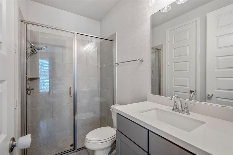 This full bathroom is located just across the private hallway of the downstairs secondary bedroom and is the perfect place for guests to get ready in while visiting or an in-law suite. It features beautiful countertops and cabinets, large mirror, and a walk-in shower with tile surround and mud set floors.